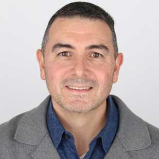 Jason smiling, wearing a a blue shirt, gray jacket